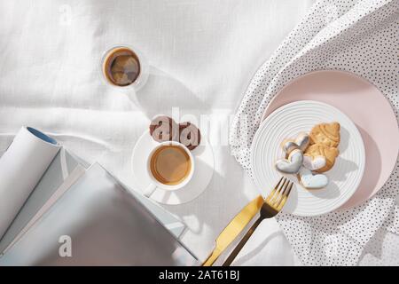 Vista dall'alto del caffè con deliziosi biscotti e riviste su tovaglia bianca Foto Stock