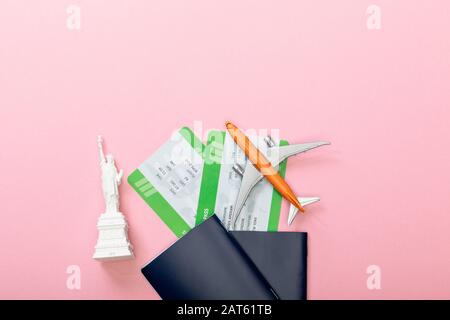 vista dall'alto dei biglietti aerei vicino ai passaporti e alla piccola statua della libertà su rosa Foto Stock