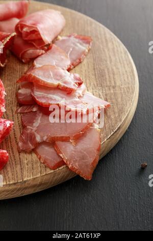 delizioso piatto di carne con prosciutto su tavola di legno su superficie nera Foto Stock