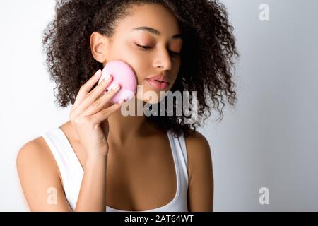 curly african american girl utilizzando spazzola per il viso in silicone, isolato su grigio Foto Stock