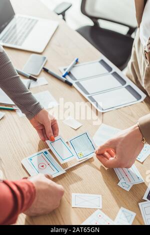 Vista ritagliata dei progettisti ux con schizzi web e protopype mobile che lavorano al tavolo Foto Stock