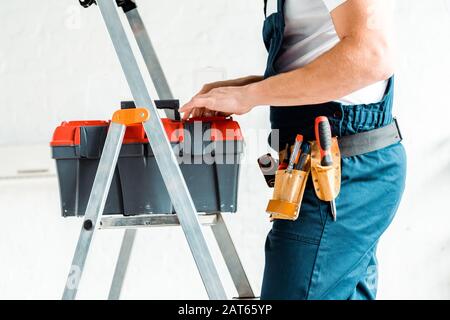 vista ritagliata dell'installatore in piedi sulla scala e sulla cassetta portautensili Foto Stock