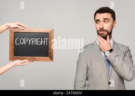 vista parziale della donna che tiene lavagna con iscrizione copyright vicino a un uomo d'affari scettico isolato sul grigio Foto Stock