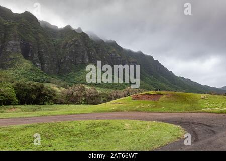 Kaaawa, Oahu, Hawaii, Stati Uniti. - 11 gennaio 2020: La strada sterrata rende un prato a U-turn ingreen con scogliere rocciose alte di colore marrone scuro a nero sul lato di Kualoa vall Foto Stock