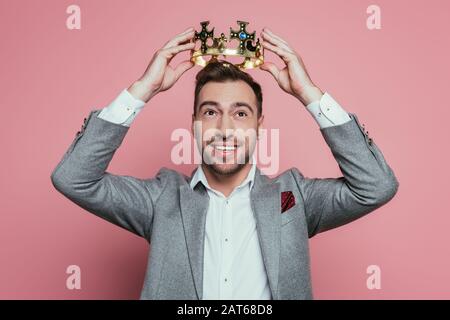 allegro uomo con bearded che indossa corona e vestito, isolato su rosa Foto Stock