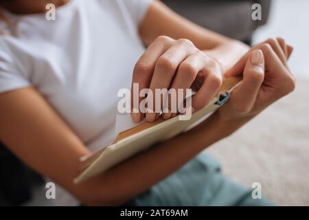 vista ritagliata di una giovane donna che tiene un libro mentre si rilassa a casa Foto Stock