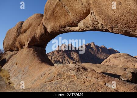 Pietra arenaria arco formazione di Spitzkoppe Erongo in Namibia con vista sulle montagne sullo sfondo Foto Stock