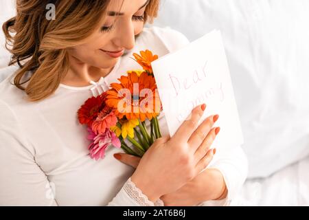 felice donna sorridente tenendo bouquet di gerberi e mamme carta da giorno Foto Stock