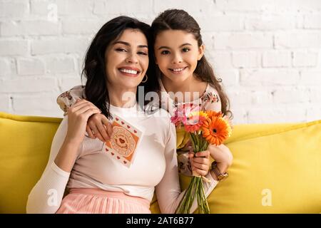 adorabile figlia che tiene le madri carta di giorno e fiori mentre abbracciando madre felice Foto Stock