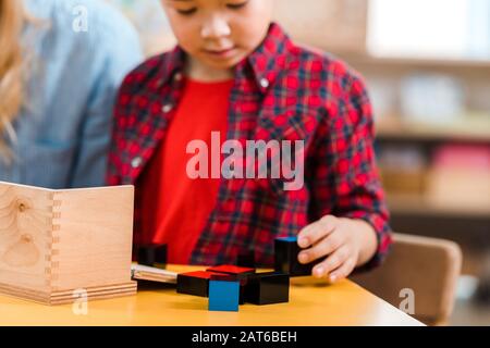 Fuoco selettivo di bambini che giocano i blocchi della costruzione accanto all'insegnante nella scuola di montessori Foto Stock