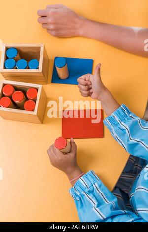 Vista ad alto angolo del bambino che mostra il pollice in su dal gioco di legno e l'insegnante nella scuola di montessori, vista corta Foto Stock