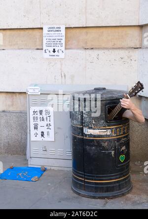 Street busker nascondendosi in bidone dei rifiuti suonando una chitarra, a Cambridge, Regno Unito Foto Stock