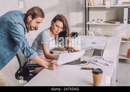 illustrator tenendo lo schizzo vicino al collega negli occhiali Foto Stock