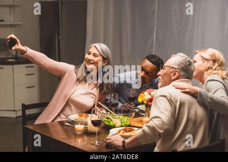 sorridendo amici multiculturali che prendono selfie con smartphone durante la cena Foto Stock