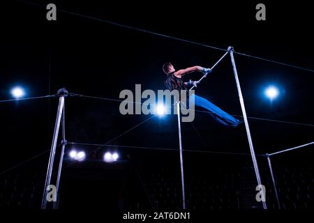 vista ad angolo basso della ginnastica eseguita su barre orizzontali in arena di circo Foto Stock