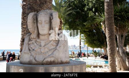 Dama de Elche replica scultura accanto a Playa de Poniente spiaggia con turisti a piedi in una giornata di sole (Benidorm, Costa Blanca, Alicante, Spagna) Foto Stock