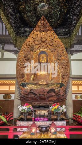 Kaneohe, Oahu, Hawaii, Stati Uniti. - 11 gennaio 2020: Buddha d'oro in posizione lotus statua in Byodo-In tempio buddista con sfondo e baldachin. Fiore Foto Stock