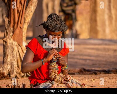 Namibia Rurale - 21 Agosto 2016. Una giovane donna in un villaggio tribale Himba che si prepara a vendere artigianato ai turisti, che è una fonte importante di reddito. Foto Stock