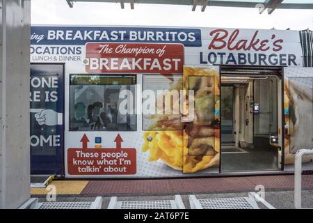 Sun link streetcar parzialmente visto fermato a riparo con porte aperte e auto esterne dipinte con divertente pubblicità sovradimensionata per la colazione burritos Foto Stock