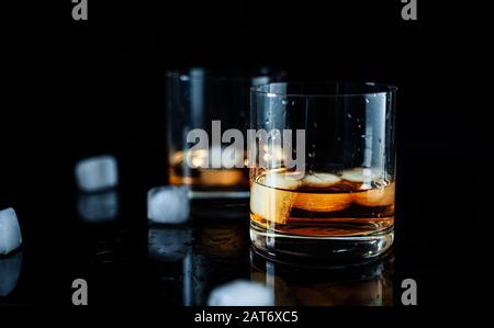 Due eleganti e semplici bicchieri di whisky di lusso con cubetti di ghiaccio su sfondo nero Foto Stock