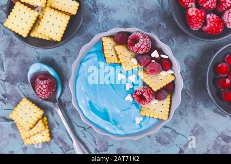 Ciotola di frullato di frutta sana tinto con polvere di spirulina blu naturale e condita con lamponi rossi e crusbery e biscotti piccoli Foto Stock