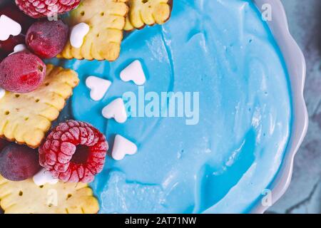 Primo piano di frutta sana ciotola frulie tinto con polvere di spirulina blu naturale e sormontato con lampone rosso e crusbery e biscotti piccoli Foto Stock