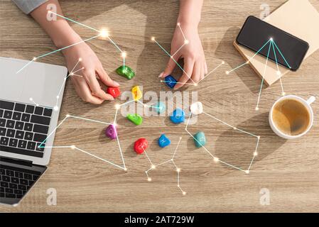 Vista dall'alto dell'astrologo che tiene pietre con segno zodiaco accanto a laptop, caffè e costellazioni Foto Stock