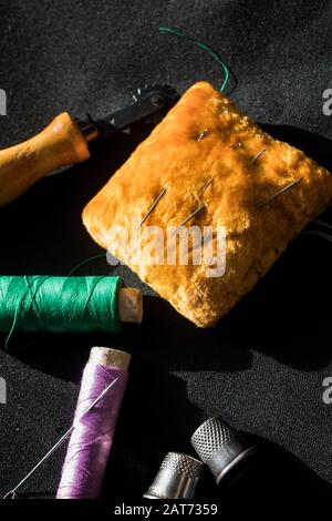 Accessori per cucire su sfondo nero. Fili per cucire, aghi, pincushion e ditali per cucire. Foto Stock