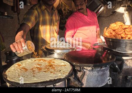 In una stalla di cibo a Mumbai, India, un cuoco fa Masala Dosa, un piatto indiano popolare, speziando le spezie sulla pastella. Destra: Una ciotola di Vade / Vadas Foto Stock