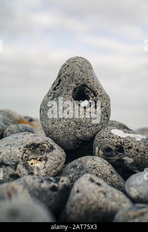 Colpo di closeup verticale di una roccia di ghiaia con un buco su un mucchio di rocce su uno sfondo sfocato Foto Stock