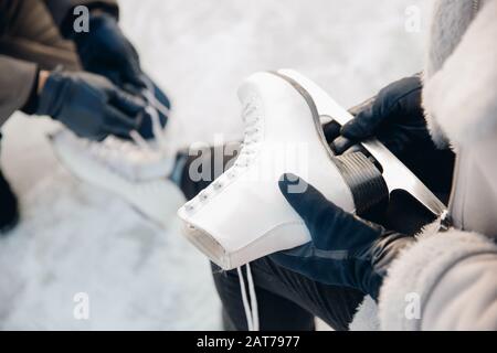 L'uomo aiuta a mettere su pattini per pista di ghiaccio neve a ragazza, concetto di vacanza invernale, riposo di famiglia Foto Stock