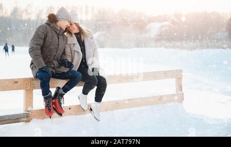 Attività invernali all'aperto. Amorevole coppia ragazza e giovane uomo pista di pattinaggio su ghiaccio, in background luce del sole Foto Stock