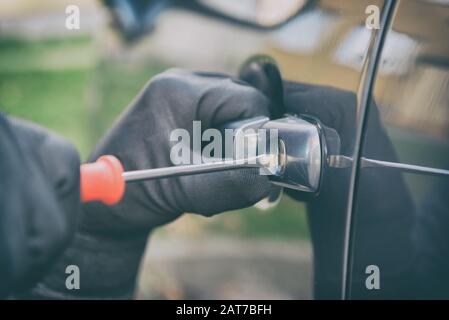 Ladro in guanti neri apre la vettura con un cacciavite Foto Stock
