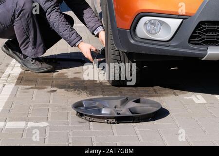 L'uomo sta cambiando la ruota dopo un guasto di automobile. Pneumatico della vettura danneggiato. Equilibratura o riparazione delle ruote e sostituzione del pneumatico della vettura. Concetto di riparazione automatica. Foto Stock