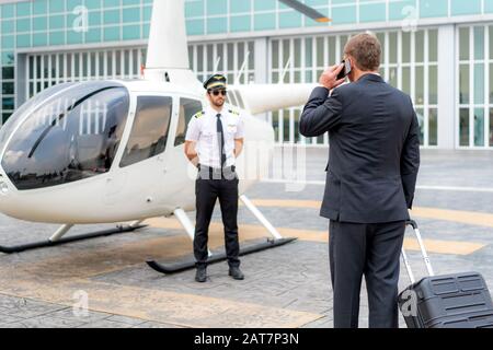 Uomo D'Affari anziano manager con bagagli che parlano telefono cellulare e a piedi per l'elicottero alla partenza a destinazione a eliporto in aeroporto con helicop Foto Stock