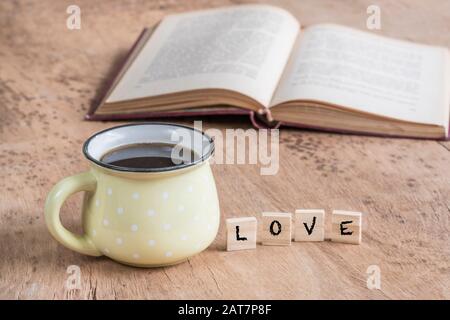 tazza di caffè e parola d'amore su un tavolo di legno contro il libro Foto Stock