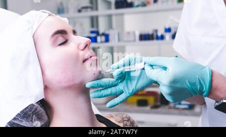 Il medico estetista femminile che fa l'iniezione in faccia giovane donna. Il medico cosmetologo che esegue la procedura di contornazione del viso. Concetto di salone di bellezza Foto Stock