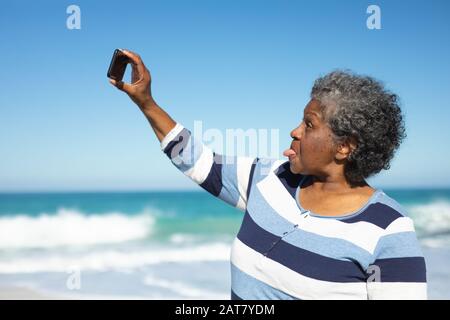 Vecchia donna che prende selfie alla spiaggia Foto Stock