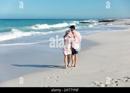 Vista posteriore della giovane coppia che abbraccia la spiaggia Foto Stock