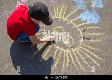 Il ragazzo disegna con gesso sul pavimento il sole.Children's Street art futuro artista. Picaksso Piccolo. Foto Stock