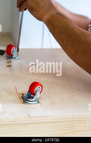 Fissaggio ruota orientabile su legno compensato, mobili. Foto Stock