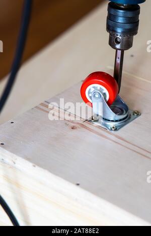 Fissaggio ruota orientabile su legno compensato, mobili. Foto Stock