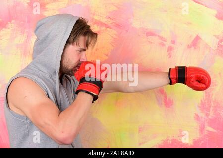 Sport box e concetto di lotta. Boxer con treni viso concentrati per colpire. Il ragazzo in felpa con cappuccio grigio senza maniche indossa guanti da boxe in pelle rossa. Uomo con mes