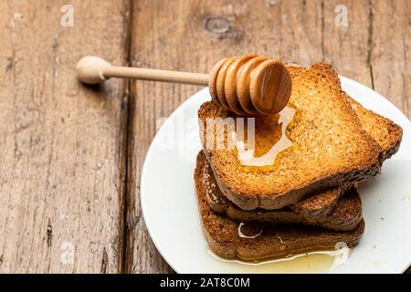 Cucchiaia di miele appoggiata su alcuni fette biscottate integrali sul tavolo. Foto Stock