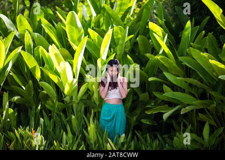 Giovane donna in piedi nella foresta pluviale con lussureggiante verde fogliame. Foto Stock