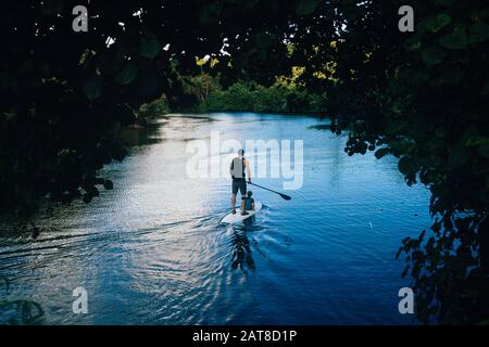 Vista ad alto angolo dell'uomo e del suo figlio pagaia imbarco lungo un fiume giungla. Foto Stock