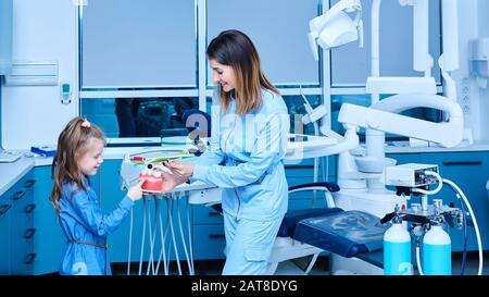 Dentista pediatrico che mostra i principi fondamentali di igiene dentale. Dentista pediatrico femminile che mostra un trattamento per adorabile bambina in un ospedale Foto Stock