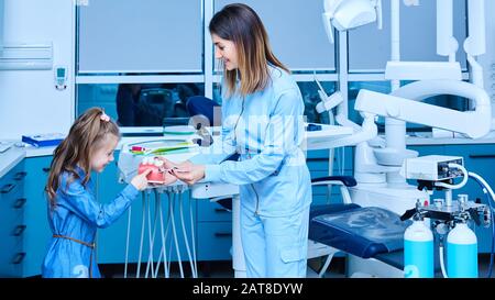 Dentista pediatrico che mostra i principi fondamentali di igiene dentale. Dentista pediatrico femminile che mostra un trattamento per adorabile bambina in un ospedale Foto Stock