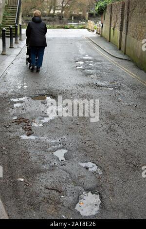 buche piene d'acqua su una strada a richmond sul tamigi, surrey, inghilterra, mentre una donna spinge un buggy verso il tamigi Foto Stock