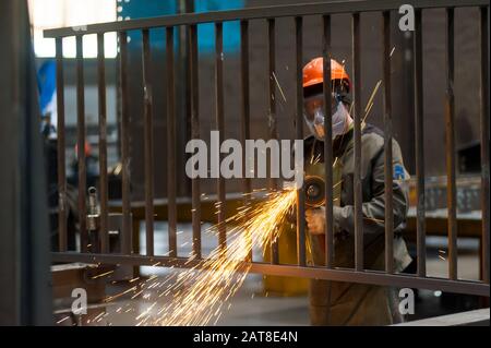 Tyumen, Russia - 4 Settembre 2019: Mostootryad-36 fabbrica. Industria pesante lavoratore taglio della tubazione in acciaio con smerigliatrice angolare in officina Foto Stock